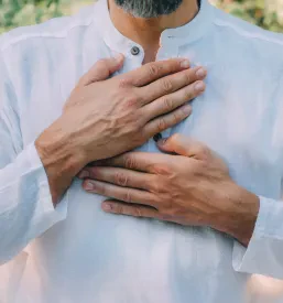Moški med reiki samozdravljenjem drži roke nad srčno čakro. Osredotoča se na energijo in notranji mir.
