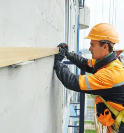 Gradbenik skrbno meri in preverja nivo med delom na prezračevalni fasadi, kar zagotavlja natančnost pri projektih fasade in knauf suhomontaže Celje in okolica.
