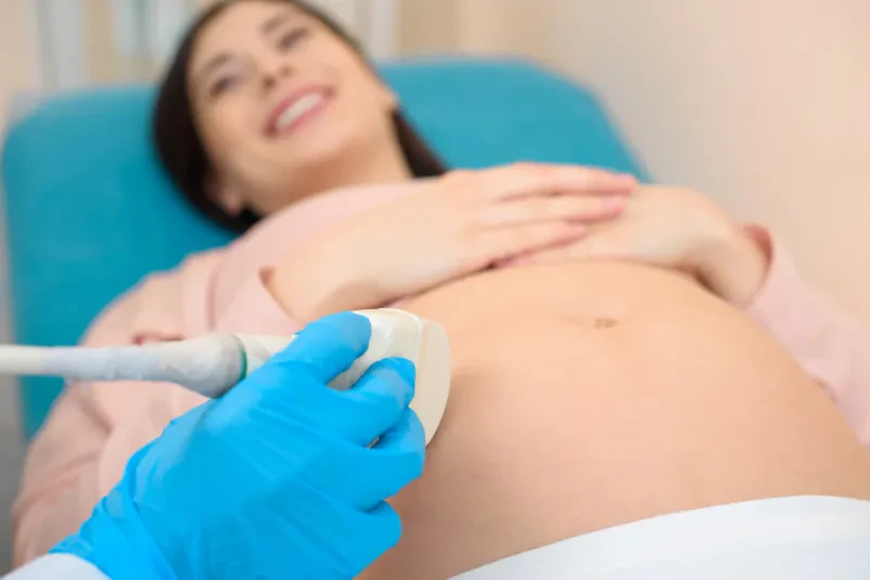 Ultrazvočni pregled pri nosečnici Ginekologinja med ultrazvočnim pregledom trebuha nosečnice, kjer lahko opazuje razvoj plodu. Postopek je ključen za spremljanje zdravja matere in otroka.