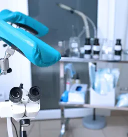 Prikaz ginekološke sobe, opremljene z modernim ginekološkim stolom in potrebno medicinsko opremo. Soba je urejena in čista, pripravljena za sprejem pacientk.