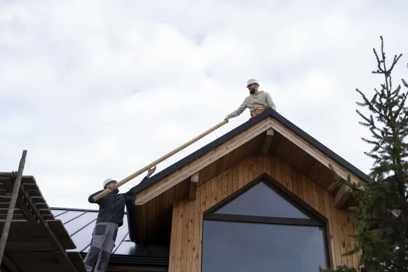 Skupina izkušenih krovcev v zaščitni opremi skrbno postavlja streho, s čimer izvajamo krovska, kleparska dela Medvode na terenu.