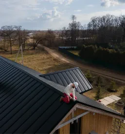 Delavec v zaščitni čeladi dela na strehi družinske hiše, ki dobiva nove strešne kritine za dolgotrajno zaščito.