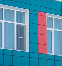 Del stene sodobne stavbe s parom velikih oken in barvnimi aluminijastimi ploščicami. Takšne kvalitetne prezračevalne fasade Slovenija združujejo funkcionalnost in privlačen dizajn.