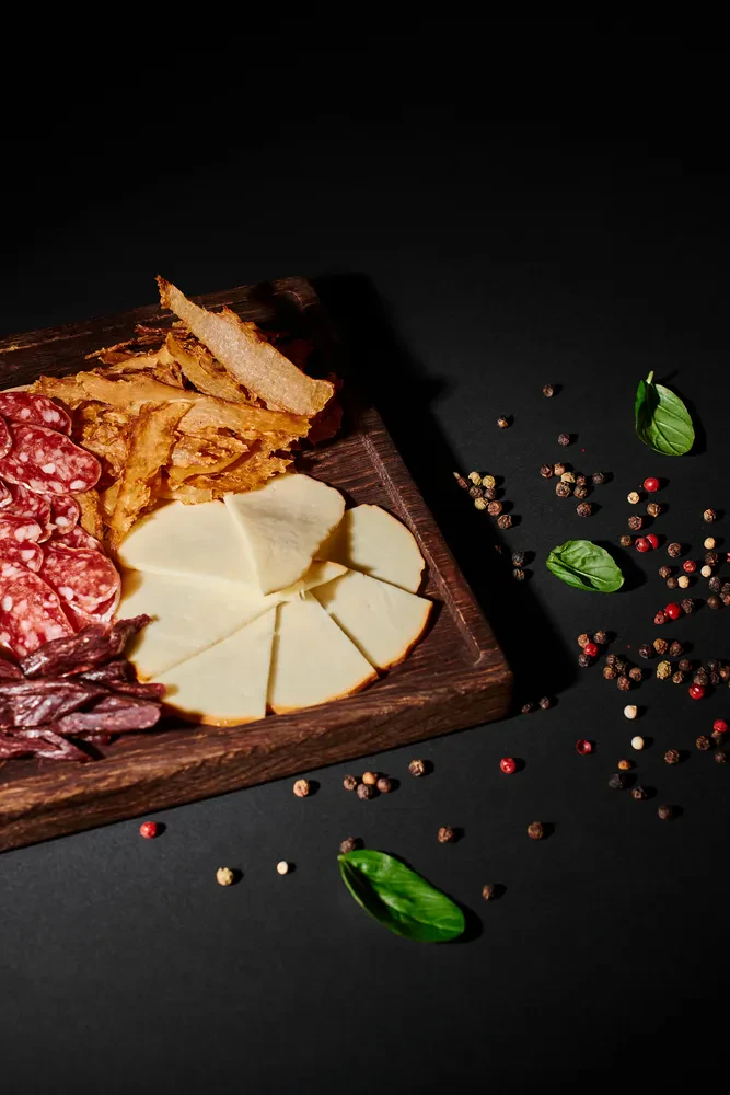 Gurmanska mesna plošča z izbranimi siri Privlačna mesna plošča z narezano sušeno govedino, rezinami salame in raznovrstnimi siri, servirana na temni podlagi.