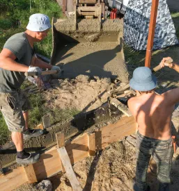 Gradbeni delavci vlivajo svež beton v leseni opaž, kar je pomemben korak pri gradnji in obdelavi lesa na gradbišču.
