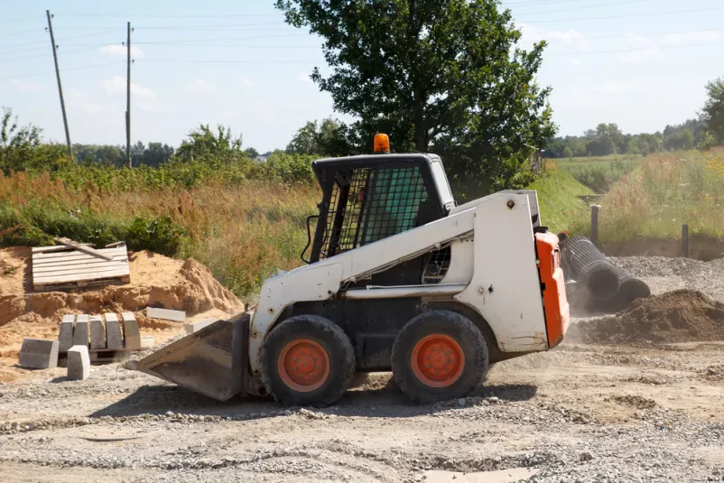 Mini bager Bobcat pri delu Rumeni mini bager Bobcat marljivo dela na gradbišču, kjer se pripravlja teren za novo cesto.
