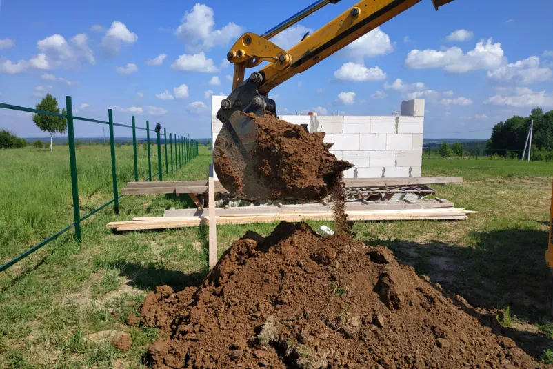 Rumeni bager koplje jarek Ta rumeni bager spretno koplje globok jarek v zemlji, kar je pogosto del storitev za mini gradbene izkope Štajerska.