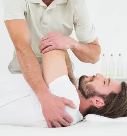 Moški fizioterapevt nežno razteza roko mladega pacienta v kliniki, s čimer izboljšuje gibljivost in pospešuje okrevanje.