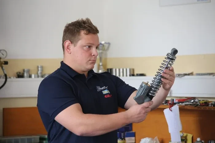 Mehanik skrbno namešča ali pregleduje komponente podvozja na dvignjenem vozilu. Pomemben del servisa in obnove.