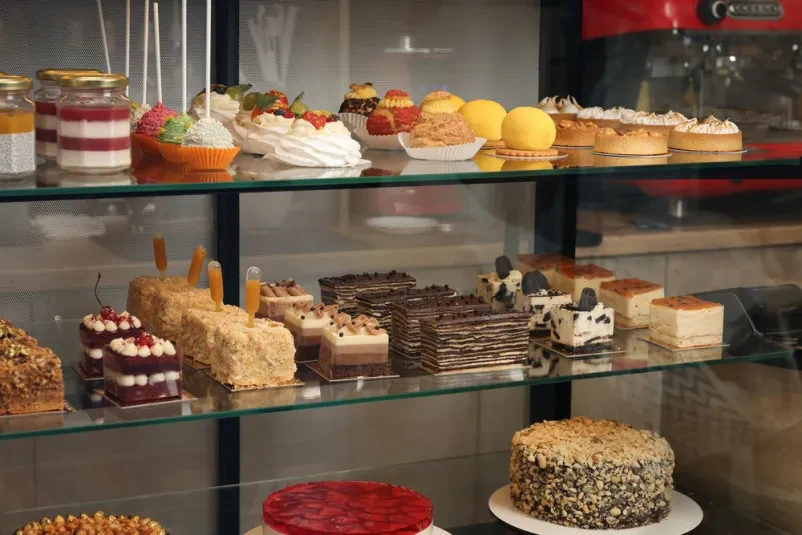 Raznolika ponudba okusnih sladic Očarljiva vitrina, polna raznolikih in pisanih sladic, kot so torte in piškoti, pripravljenih za zadovoljstvo kupcev.