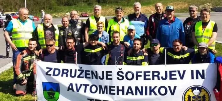 Udeleženci se zbirajo pred avtomobili na poligonu, kjer poteka praktično izobraževanje za varno vožnjo in prometno varnost.