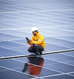 Strokovnjak z laptopom nadzoruje in upravlja proizvodnjo električne energije v sončni elektrarni, optimizirajoč delovanje sistema za maksimalno učinkovitost.