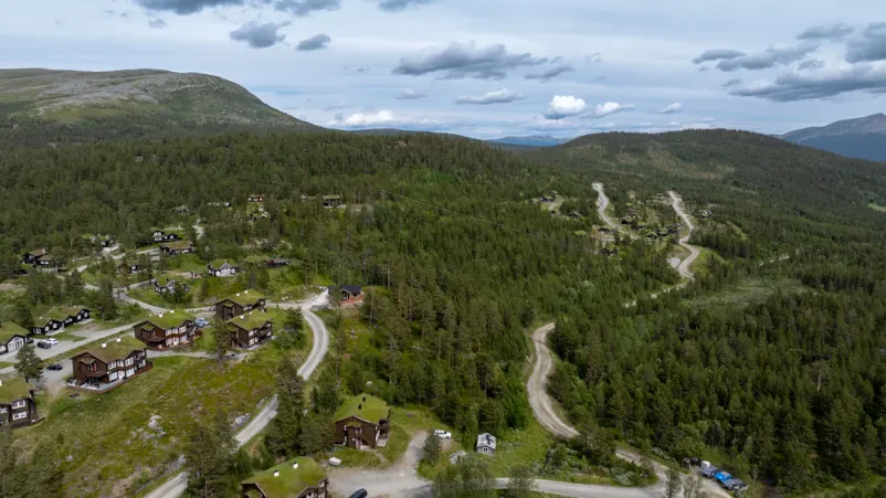Panoramski pogled iz zraka na skupino tradicionalnih lesenih koč s travnatimi strehami, obdanih z borovimi gozdovi in slikovito gorsko pokrajino, idealno za nastanitev.