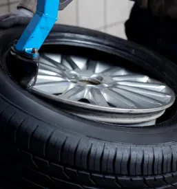 Povečan posnetek avtomehanika, ki z ročnim orodjem spretno namešča avtomobilsko pnevmatiko na platišče, kar poudarja natančnost in pozornost do detajlov pri delu.