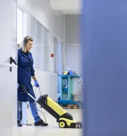 Profesionalna čistilka z učinkovitim strojem za pranje tal temeljito čisti tla v velikem industrijskem objektu.