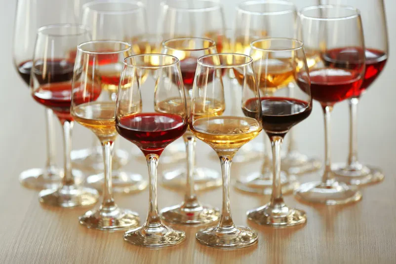 Vrsta različnih vinskih kozarcev Urejena vrsta praznih vinskih kozarcev na elegantni mizi, pripravljenih za pokušino različnih vrst vina. Odsev svetlobe poudarja kristalno čistočo posodja.