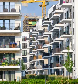Pogled na novo stanovanjsko sosesko z modernimi apartmajskimi stavbami, ki imajo čiste in urejene fasade pod jasnim nebom.