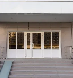 Vhodna avla stanovanjskega bloka z modernim kovinskim nadstreškom in dostopno klančino. Zagotavlja zaščito pred vremenom.