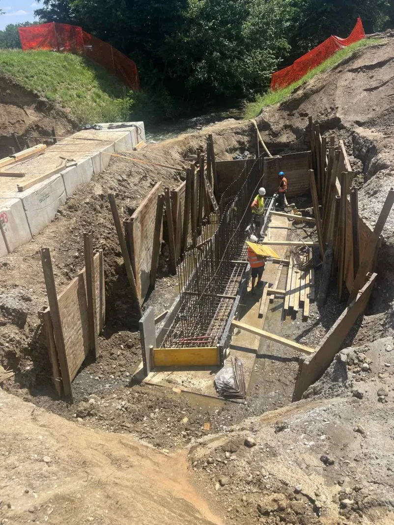Zemeljska dela z bagrom na gradbišču Velik rumen bager med izkopnimi deli na gradbišču, ki pripravlja teren za nove gradbene projekte. Prikazuje začetno fazo nizke gradnje.