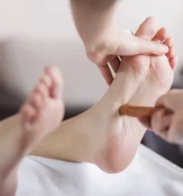 Bližnji posnetek rok, ki nežno masirajo žensko stopalo, s poudarkom na vitalnosti in naravnemu dobremu počutju. Terapija z masažo.
