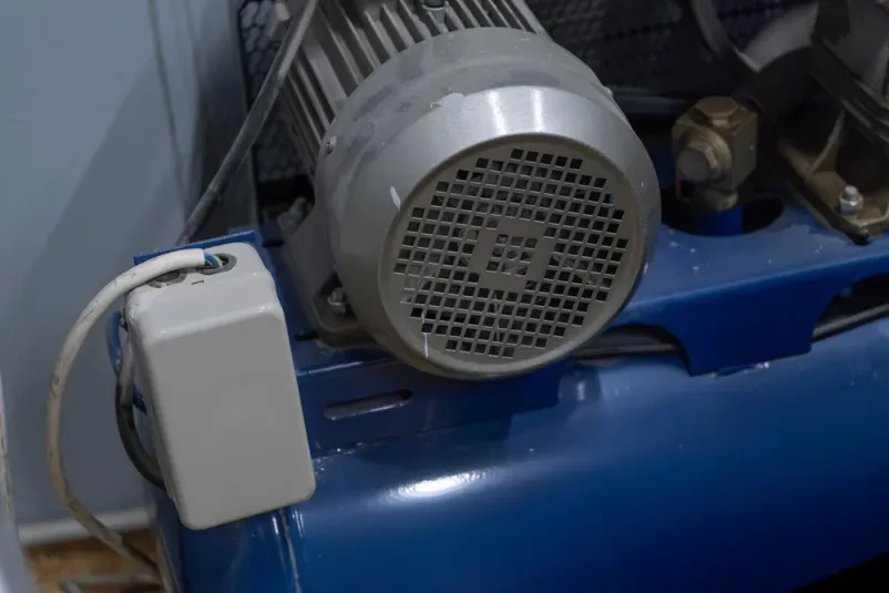 Robusten industrijski elektromotor, integriran v sistem stisnjenega zraka. Prikazuje ključno infrastrukturo za proizvodnjo in zanesljivost opreme.