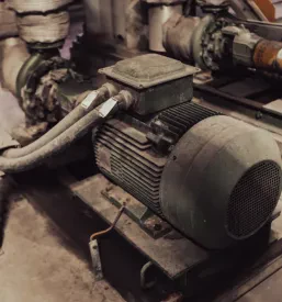 Dotrajan industrijski elektromotor, povezan s črpalko. Redni servis in vzdrževanje sta ključna za te industrijske stroje za globalni trg.