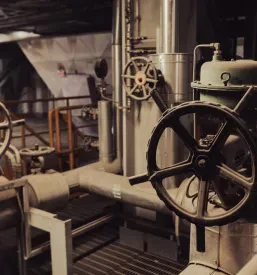 Velike industrijske cevi z ventili in aktuatorji v mehanskem objektu. Robusten nadzorni sistem uravnava pretok in tlak v industrijskih procesih.
