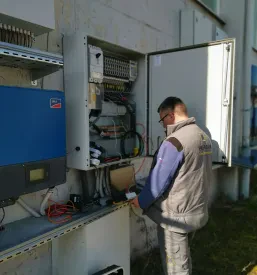 Delavec v zaščitni opremi skrbno pregleduje in pritrjuje sončne panele na nosilno konstrukcijo na strehi objekta.
