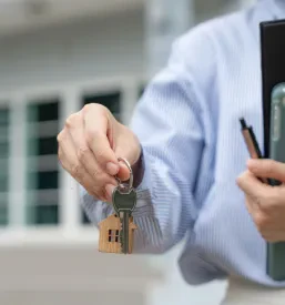 Prijazen nepremičninski agent drži ključ novega domovanja in se smehlja, pripravljen za predajo najemniku.