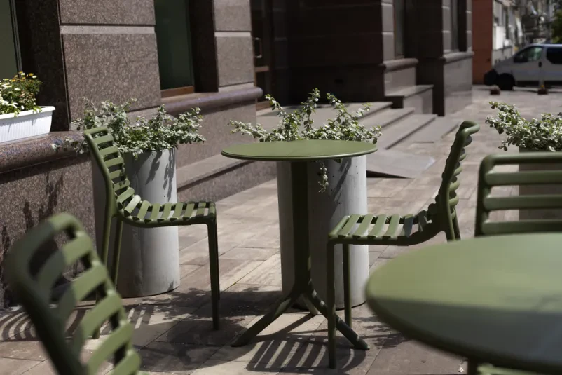 Udobni stoli in mize na prostorni letni terasi, pripravljeni za obiskovalce, ki želijo uživati v poletni odprti kavarni Domžale.