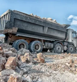 Velik nakladalec naklada razsuti gradbeni material, verjetno glino, v prostoren tovornjak v glinokopu.