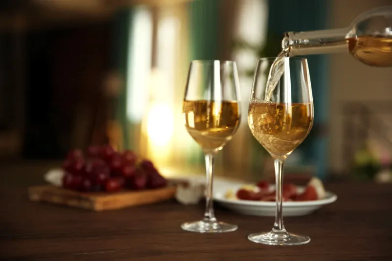 Naletavanje belega vina v kozarec Prijeten prizor nalivanja svežega belega vina iz steklenice v kozarec, pripravljenega za pokušino. Idealno za prodajo belega vina Pomurska, kjer cenimo kakovost in tradicijo.