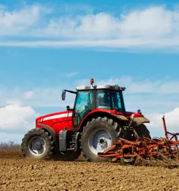 Rdeč kmetijski traktor z priključenim plugom orje oranžno polje, kar je ključnega pomena za pripravo zemlje. Potrebujete takšno opremo? Preverite prodajo in odkup kmetijskih strojev in naprav Slovenija.