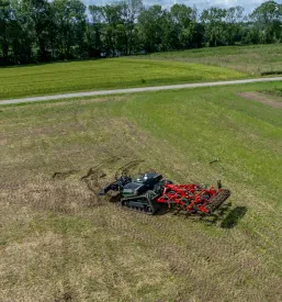 Futuristični avtonomni kmetijski robot z gosenicami in priključkom za oranje polj, ki predstavlja napredno tehnologijo v kmetijstvu.