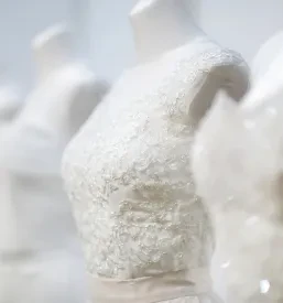 Več poročnih oblek je razstavljenih na belih lutkah, poudarjajoč različne kroje, detajle in eleganco v svetlem prostoru.