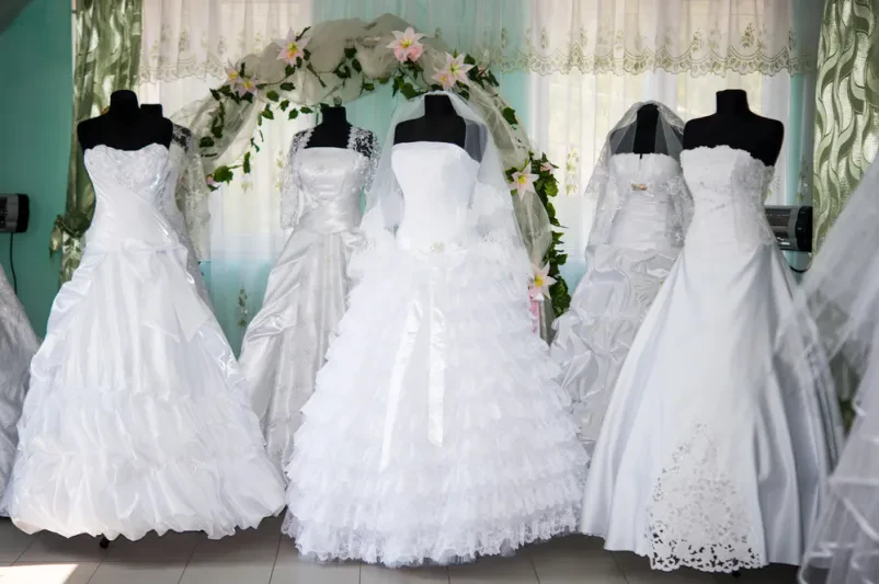 Poročne obleke v poročnem salonu Elegantne poročne obleke, obešene v svetlem poročnem salonu, čakajo na neveste za Prodajo poročnih in svečanih oblek Pomurje.