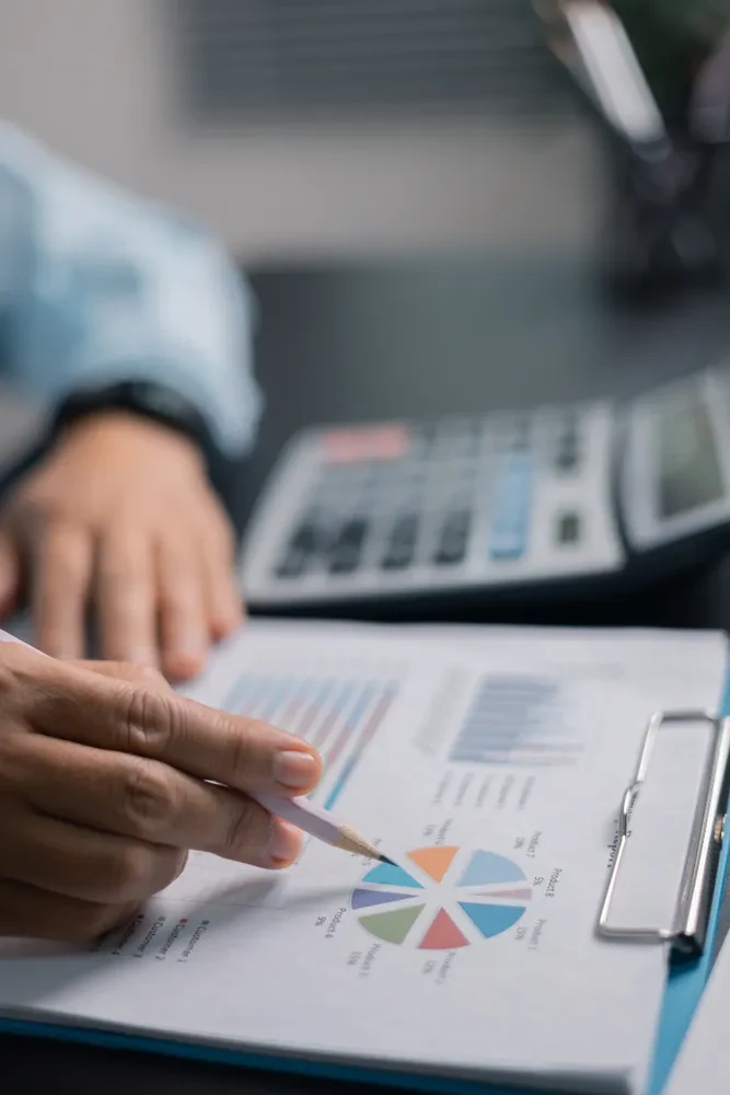 Poslovne finance in uporaba kalkulatorja Roka poslovneža, ki na mizi z dokumenti in grafi uporablja kalkulator za izračun finančnih podatkov in analizo stroškov.