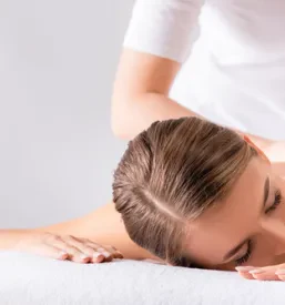 Maserka masira zadovoljno mlado žensko, ki leži na masažni mizi v spa salonu, kar je odličen primer klasične masaže za sprostitev in regeneracijo, ki jo ponujajo Športne in klasične masaže Šentjernej na Dolenjskem.