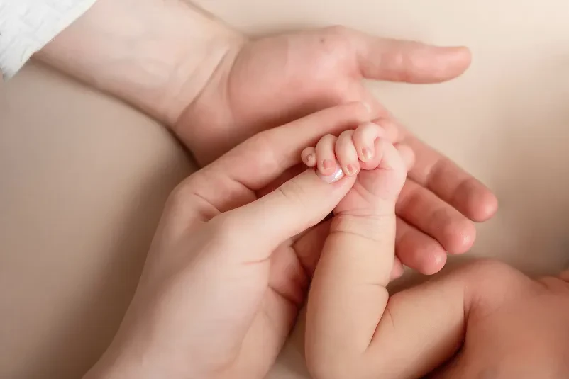 Mati in dojenček v ergonomski nosilki Mlada mati nežno drži svojega dojenčka v ergonomski nosilki, kar prikazuje tesno vez med mamo in otrokom in udobje.