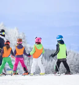 Otroci se učijo smučati z inštruktorjem. Pomembna praksa za Tečaj za učitelja smučanja Slovenija.
