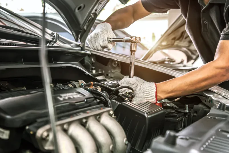 Mehanik popravlja avtomobilski motor Detajlni posnetek rok avtomehanika, ki z viličastim ključem popravlja motor v avtoservisu. To je pomemben korak za ugodno dekarbonizacijo motornih vozil v Savinjski.