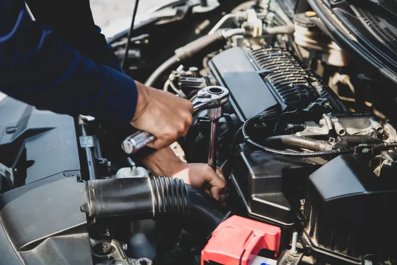 Mehanik z orodjem popravlja avto Bližnji posnetek rok avtomehanika v zaščitnih rokavicah, ki z orodjem servisira avtomobilski motor, poudarjajoč strokovnost in natančnost pri popravilu.