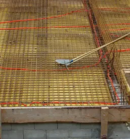 Pripravljena površina za betoniranje temeljne plošče objekta, ki je obdana z rumenimi lesenimi deskami in kovinsko mrežo.