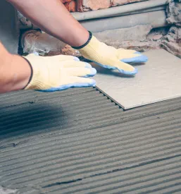 Keramičar v zaščitnih rokavicah polaga keramiko na pripravljena tla na Koroškem.