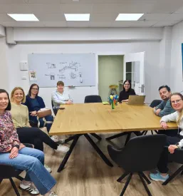 Udeleženci usposabljanja in rehabilitacije sedijo za mizo v pisarni pred tablo.