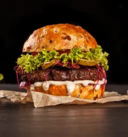 Okusni mesni burgerji s sirom in zelenjavo na leseni deski za rezanje