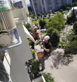 Delavec opravlja popravila na fasadi večnadstropne stavbe na večji višini.