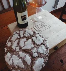 Na mizi v domačiji je hlebec kruha s flašo vina in kozarcem.