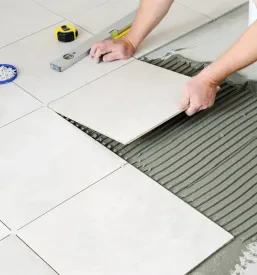 Delavec na pripravljena tla polaga bele keramične ploščice.