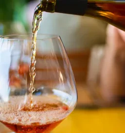 Gostinec nataka vino iz steklenice v kozarec na mizi.